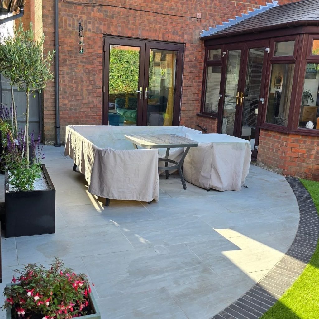 Curved grey porcelain patio beside a brick house with planters