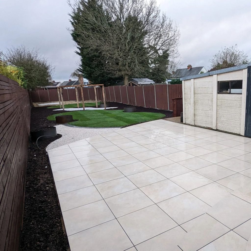 Khaki porcelain patio running alongside a dark stained slatted fence