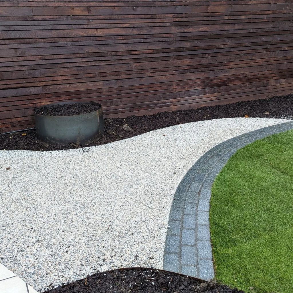 Gravel path with granite sett border alongside the lawn and a rusted planter