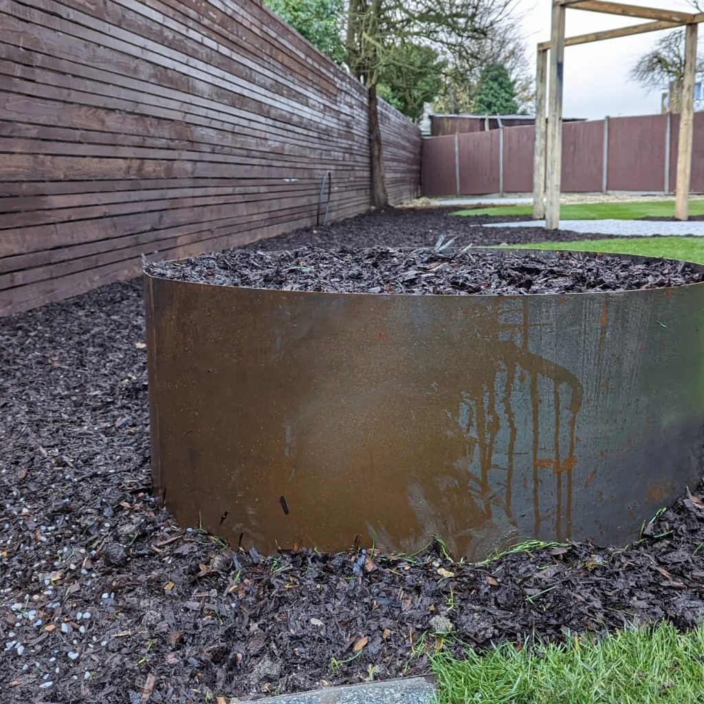 Bespoke rusted cylindrical planter against the slatted fence